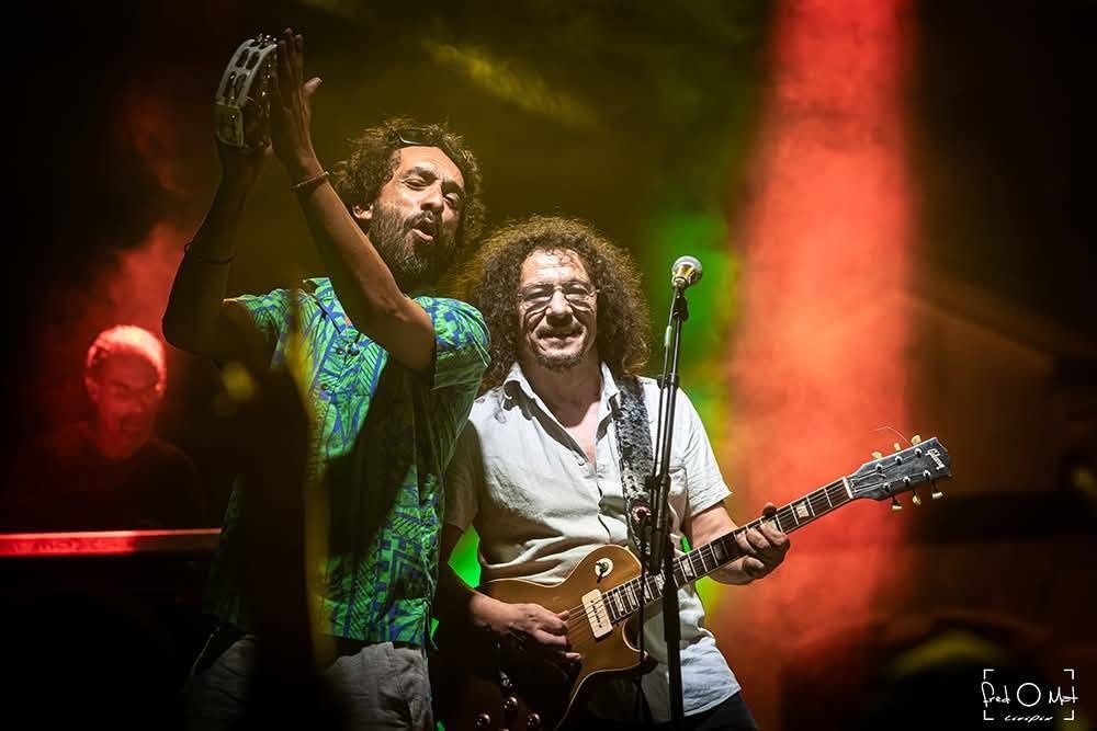 Deux musiciens de Kingston Calling, tambourin et guitare, sur fond rouge, tournée 2026